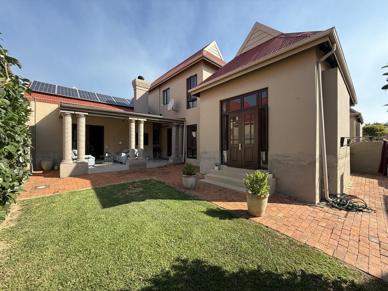 Rear view of the townhouse featuring a covered patio with columns, brick paved courtyard, small lawn, and roof-mounted solar panels.