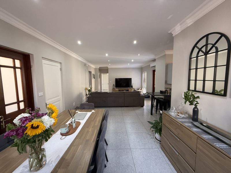 Spacious open-plan living and dining area featuring modern tiled flooring, recessed downlighting, crown molding, and a functional breakfast bar layout.