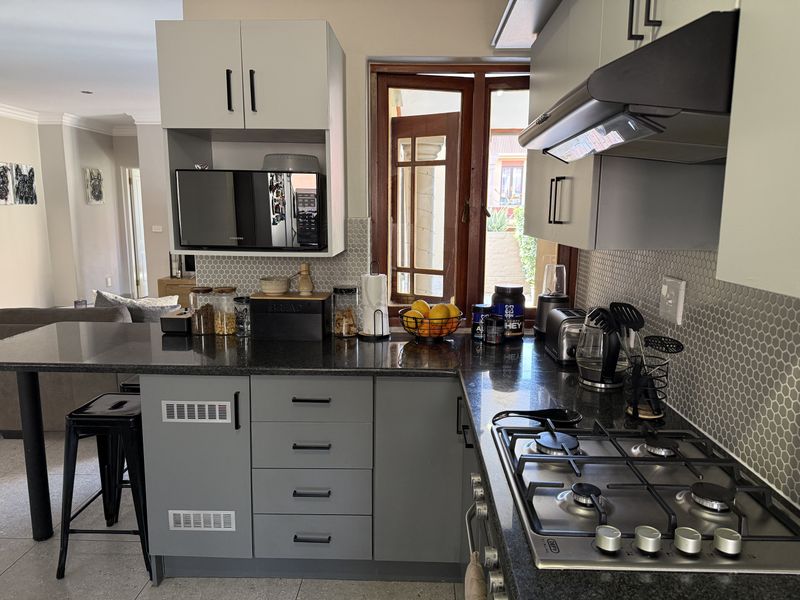 Modern kitchen featuring grey cabinetry, granite countertops, a gas hob with extractor fan, and a stylish hexagonal tiled backsplash.