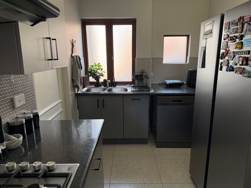 A functional kitchen featuring dark grey cabinetry, granite countertops, a gas hob, extractor fan, and a double sink with a mosaic tile backsplash.