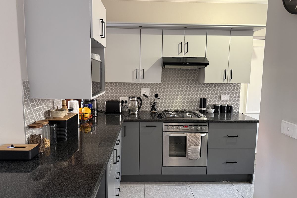 Modern kitchen featuring dark granite countertops, two-tone cabinetry, a gas hob, built-in oven, and a stylish hexagonal tiled backsplash.