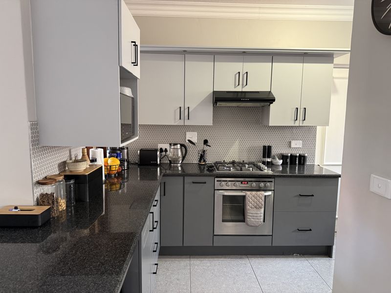 Modern kitchen featuring dark granite countertops, two-tone cabinetry, a gas hob, built-in oven, and a stylish hexagonal tiled backsplash.