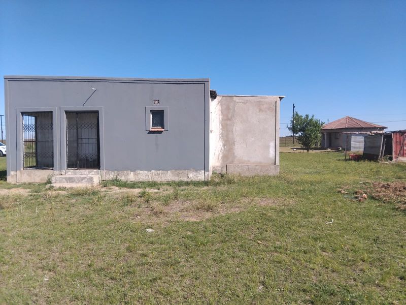 Rear view of a single-story house featuring grey painted walls, security gates, and an unfinished plaster section on the side elevation.