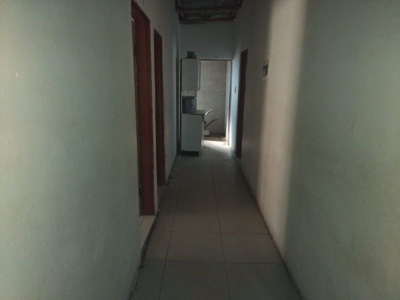 A narrow, dimly lit hallway with tiled flooring and multiple internal doors, leading towards an unfinished utility area.
