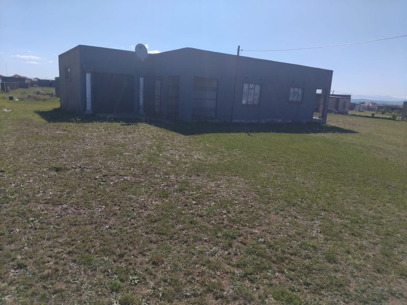 A detached single-story house featuring a concrete facade with security bars on windows, set on a large, open plot of land.