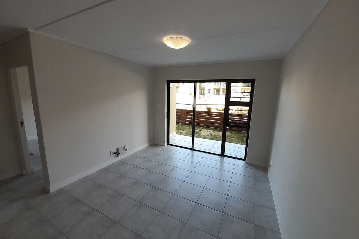 A bright, empty living room featuring neutral tiled flooring and a sliding glass door that opens onto a private patio area.