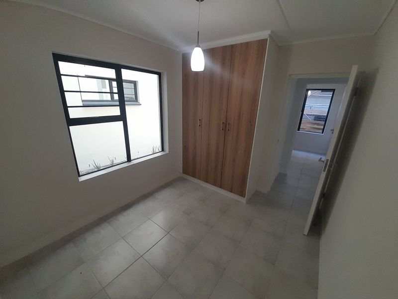A clean, empty bedroom featuring modern built-in cupboards, neutral tiled flooring, and aluminium window frames with security bars.