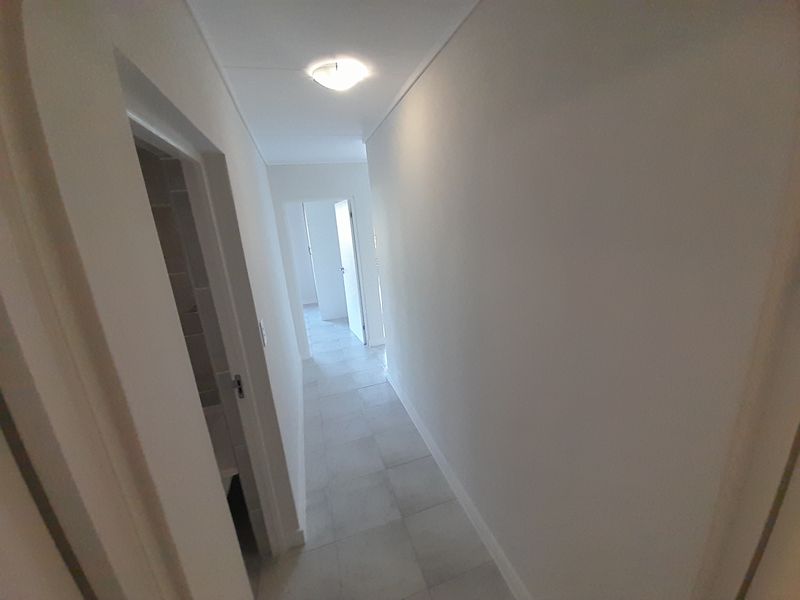 A clean, neutral hallway featuring light-colored floor tiles and access to multiple rooms, providing a bright and functional transition space within the apartment.