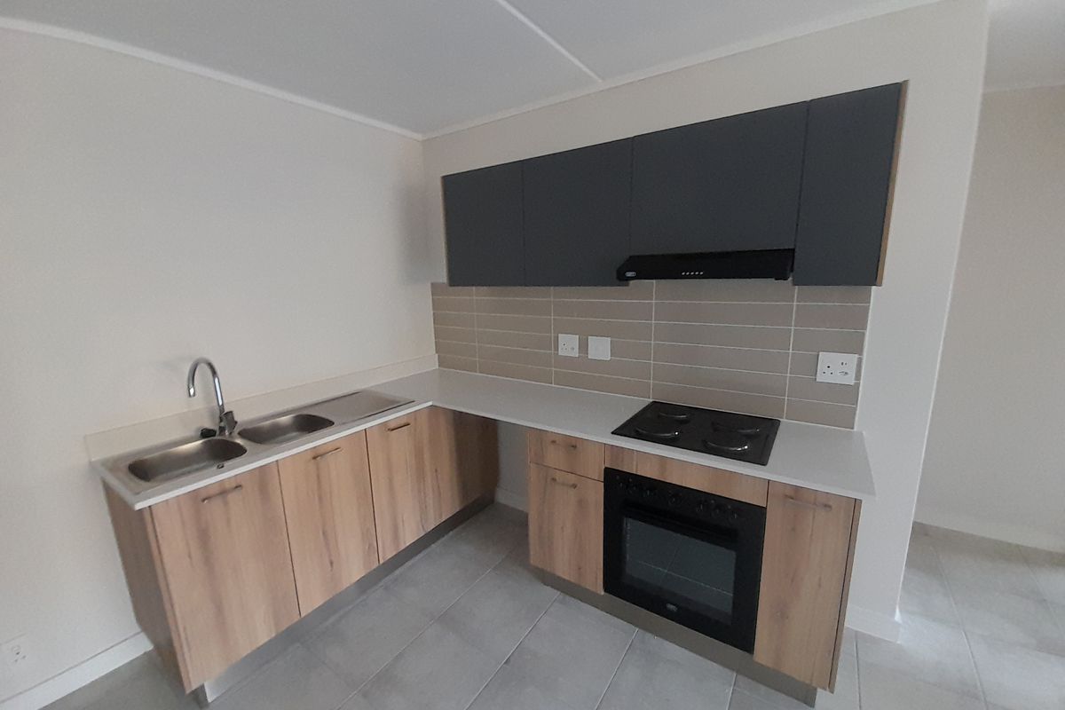 Modern kitchen featuring light wood-finish cabinetry, dark grey overhead cupboards, stone countertops, integrated oven, electric hob, and a double sink with tiled backsplash.