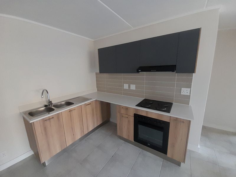 Modern kitchen featuring light wood-finish cabinetry, dark grey overhead cupboards, stone countertops, integrated oven, electric hob, and a double sink with tiled backsplash.