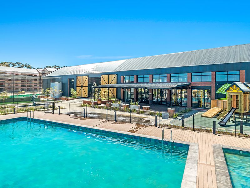 A well-maintained communal pool area featuring timber decking, a wading pool, and modern architectural building design with large glass windows and brick accents.