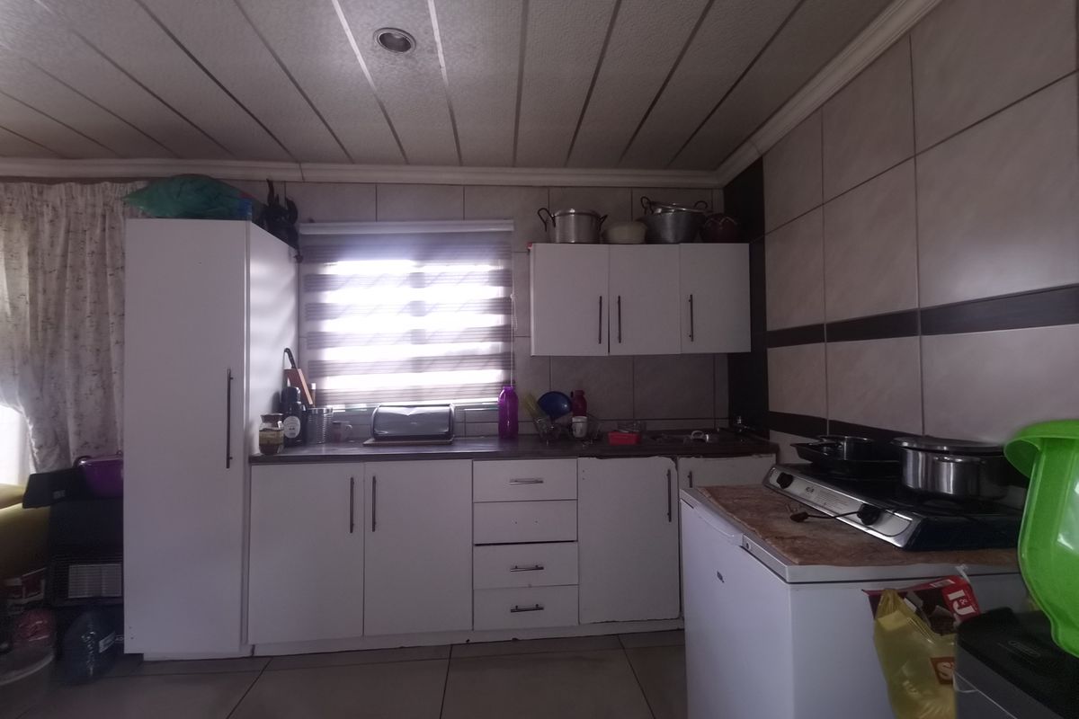 A functional kitchen featuring white built-in cabinetry, tiled splashbacks, and a gas hob, offering a practical layout with potential for modern updates.