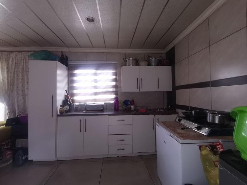A functional kitchen featuring white built-in cabinetry, tiled splashbacks, and a gas hob, offering a practical layout with potential for modern updates.