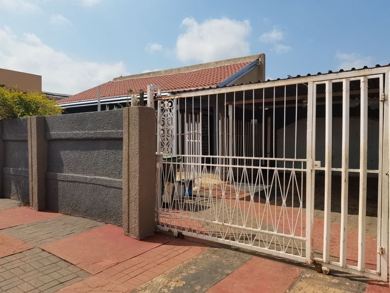 Front view of the property featuring a metal security gate, perimeter wall, and paved driveway leading to the entrance.