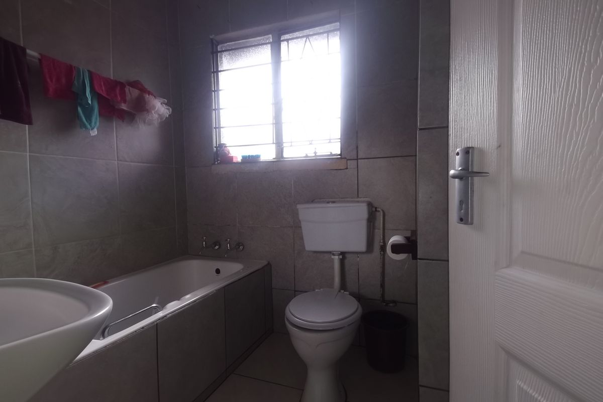 A functional bathroom featuring a bathtub, toilet, and washbasin with neutral wall and floor tiling, providing a practical space for daily use.