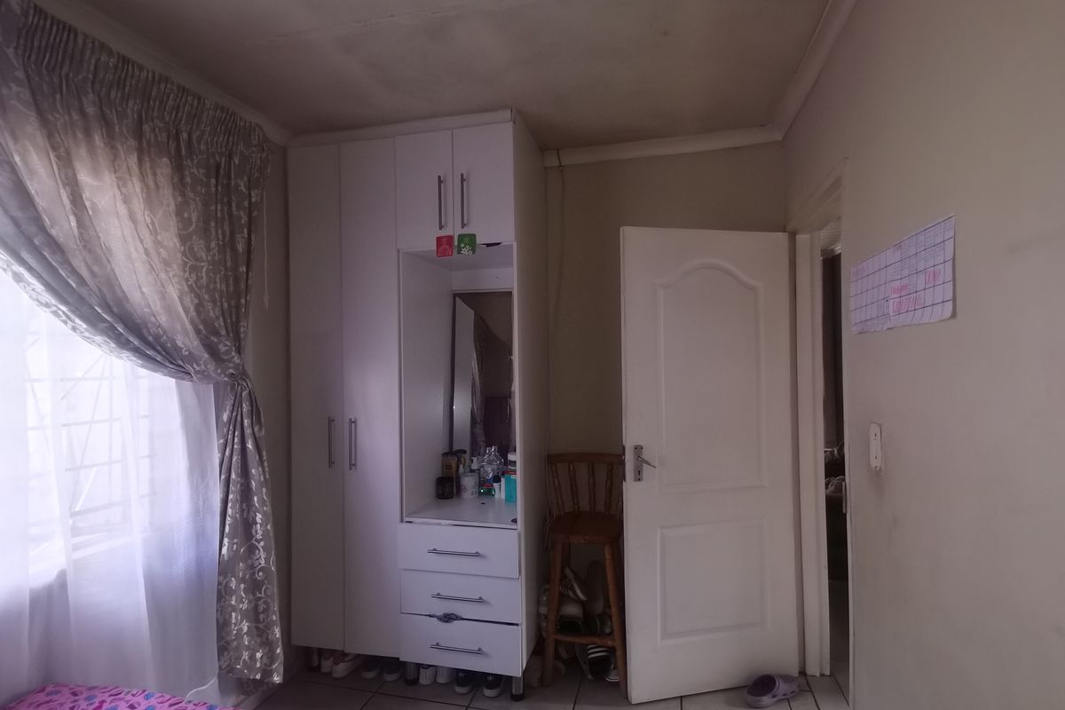A bedroom featuring a white built-in wardrobe with integrated vanity, tiled flooring, and a standard internal door.