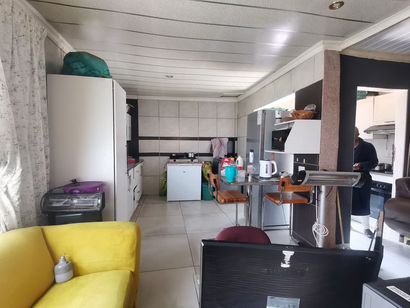 Open-plan living and kitchen area featuring tiled flooring, built-in cabinetry, and a tiled splashback, offering a functional layout with potential for modern updates.