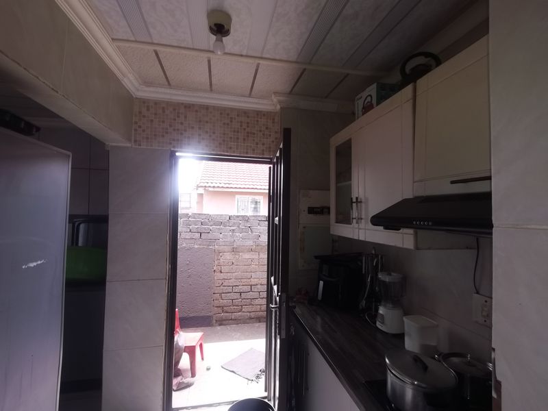 A compact kitchen featuring built-in cabinetry, a dark laminate countertop, and an extractor fan, with direct access to an outdoor area.