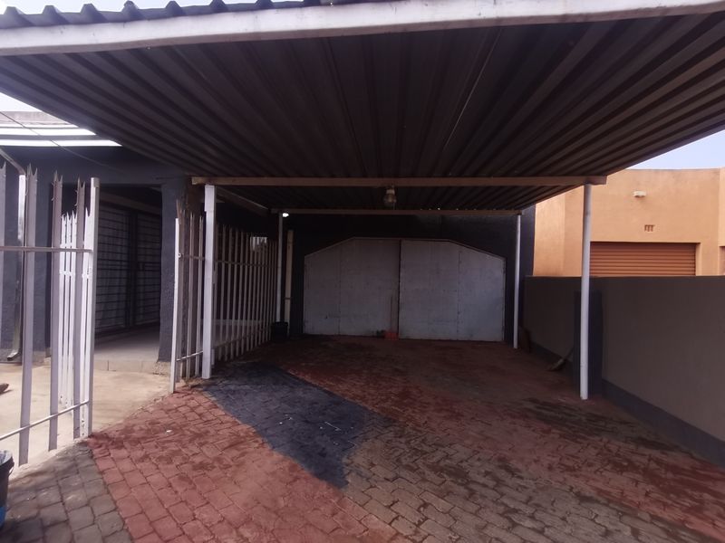 A covered carport area featuring a corrugated metal roof, paved driveway, and secure metal garage doors, providing sheltered off-street parking.