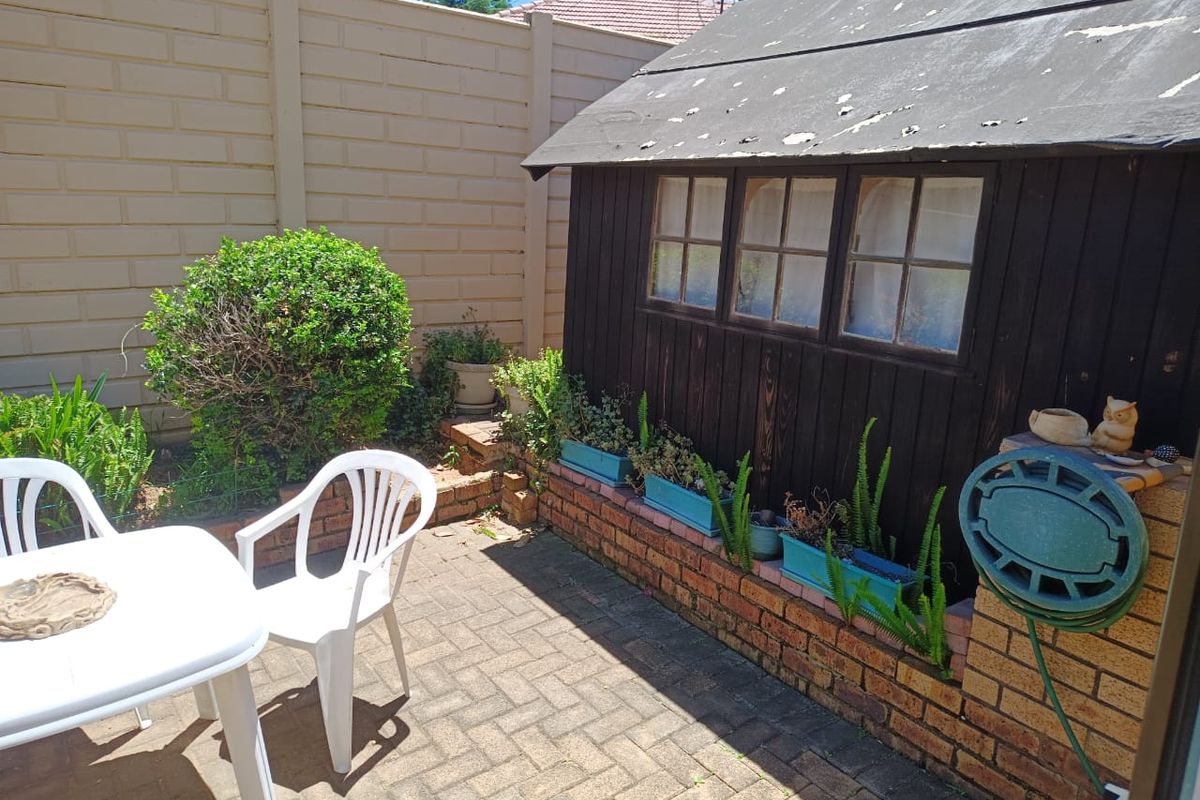 A rear courtyard area featuring brick paving, a precast boundary wall, and a timber garden shed requiring maintenance.