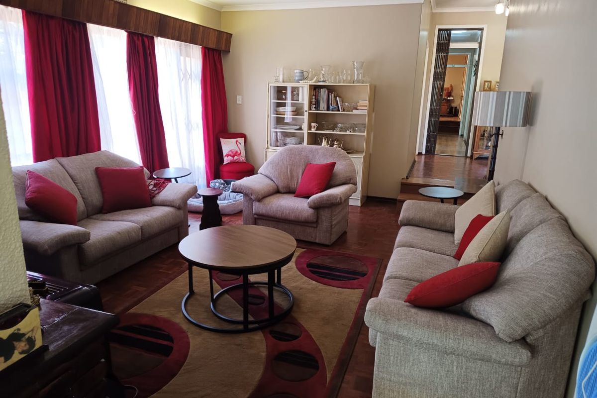 A spacious living room featuring classic parquet flooring, a wooden pelmet, and large sliding doors that provide access to the exterior.