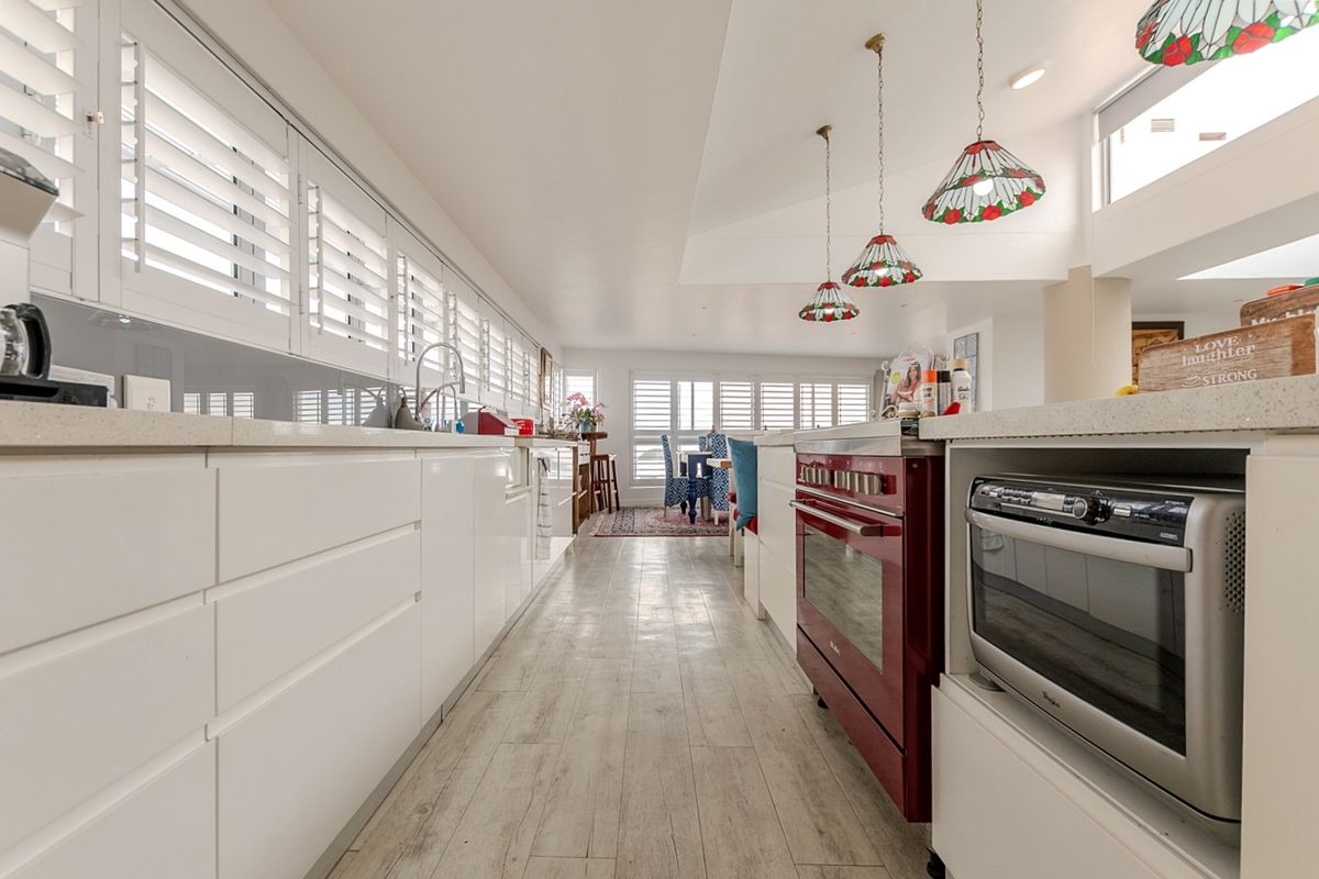 Modern kitchen featuring white cabinetry, stone countertops, a distinctive red range oven, built-in microwave, and plantation shutters, creating a bright and functional culinary space.