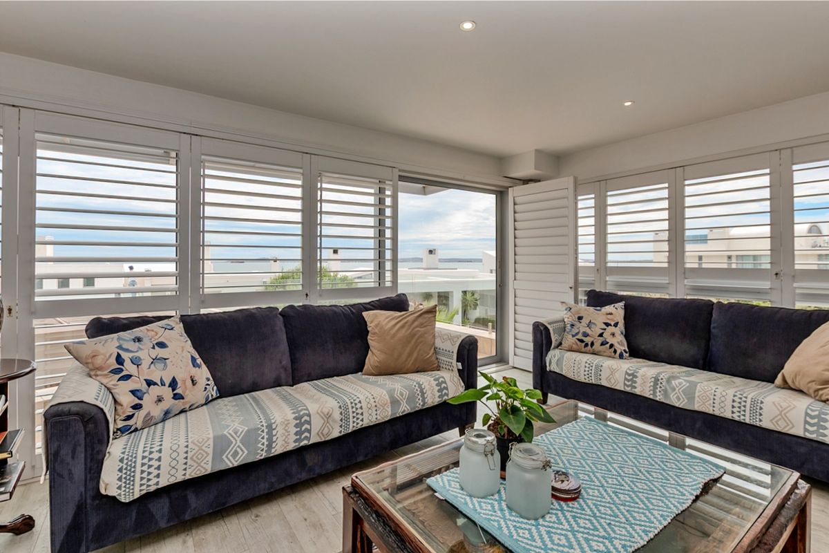 A bright living room featuring plantation shutters, recessed lighting, and sliding glass doors that open to an outdoor area with coastal views.