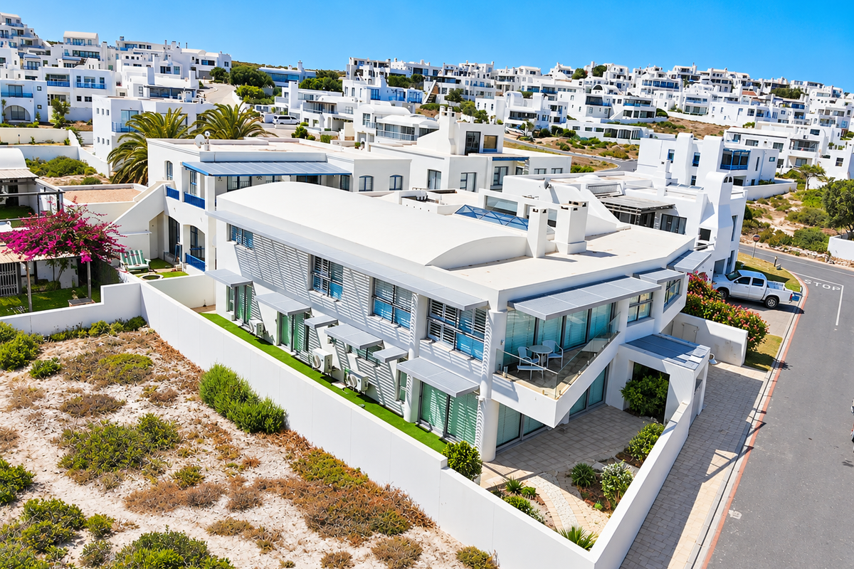 An aerial view of a modern white multi-level residential property featuring a curved roof, balconies, and a private paved courtyard within a coastal estate.
