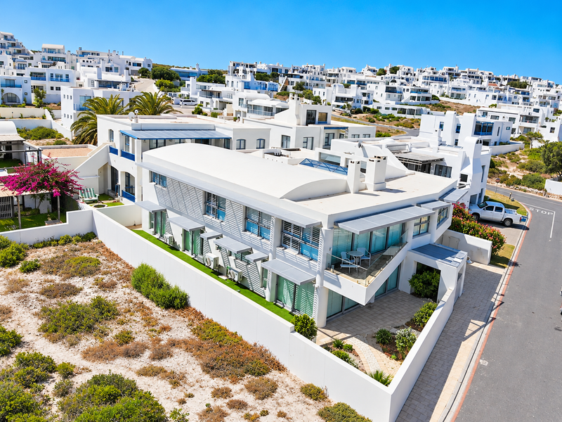 An aerial view of a modern white multi-level residential property featuring a curved roof, balconies, and a private paved courtyard within a coastal estate.