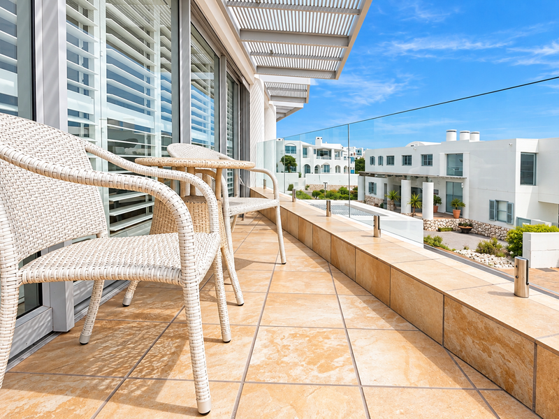 A spacious, well-maintained balcony featuring tiled flooring, a modern glass balustrade, and sliding glass doors with integrated shutters, offering a bright outdoor living space.