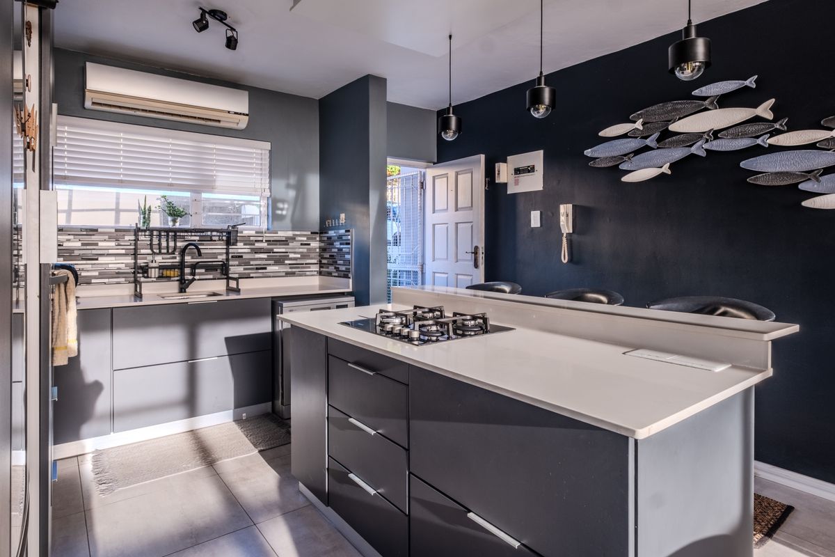 Modern kitchen featuring a central island with gas cooktop, sleek grey cabinetry, stone countertops, and contemporary pendant lighting in an open-plan layout.