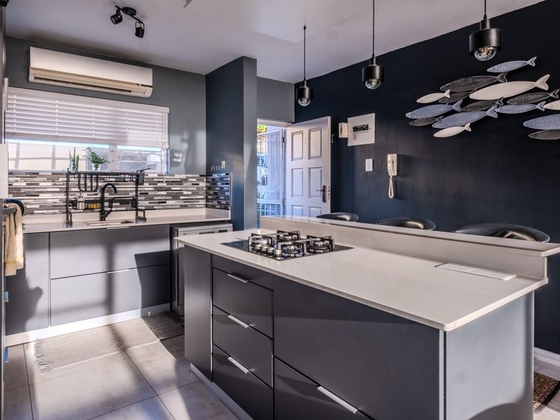 Modern kitchen featuring a central island with gas cooktop, sleek grey cabinetry, stone countertops, and contemporary pendant lighting in an open-plan layout.