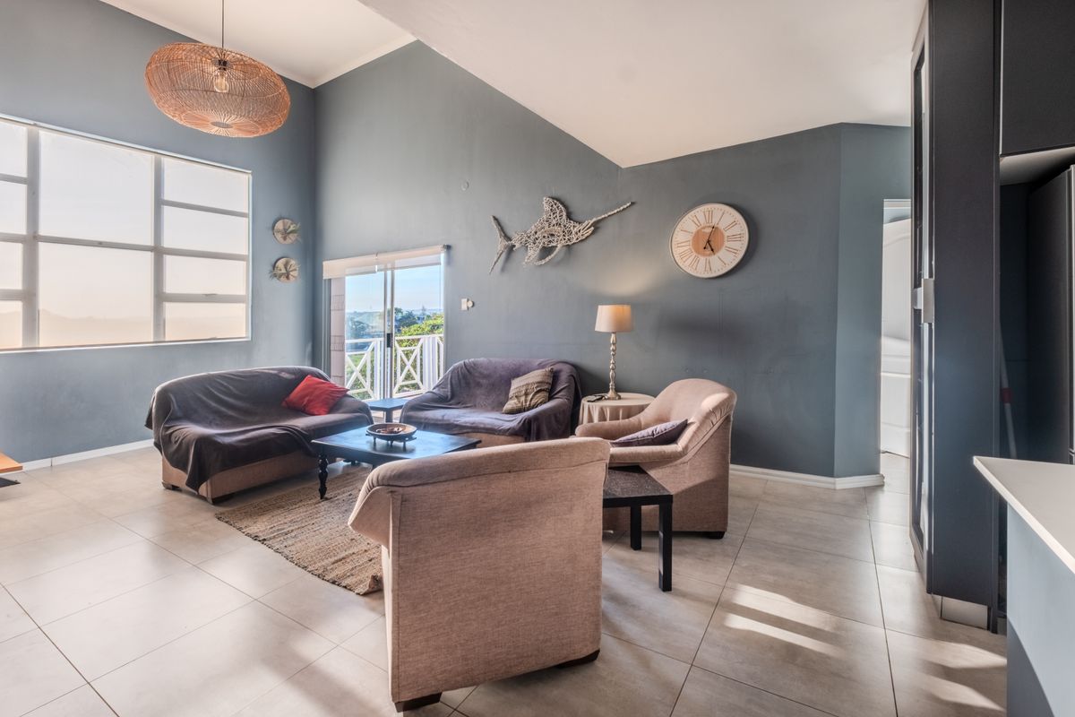 Spacious living room featuring vaulted ceilings, tiled flooring, and large windows with access to a balcony, offering a bright and open atmosphere.