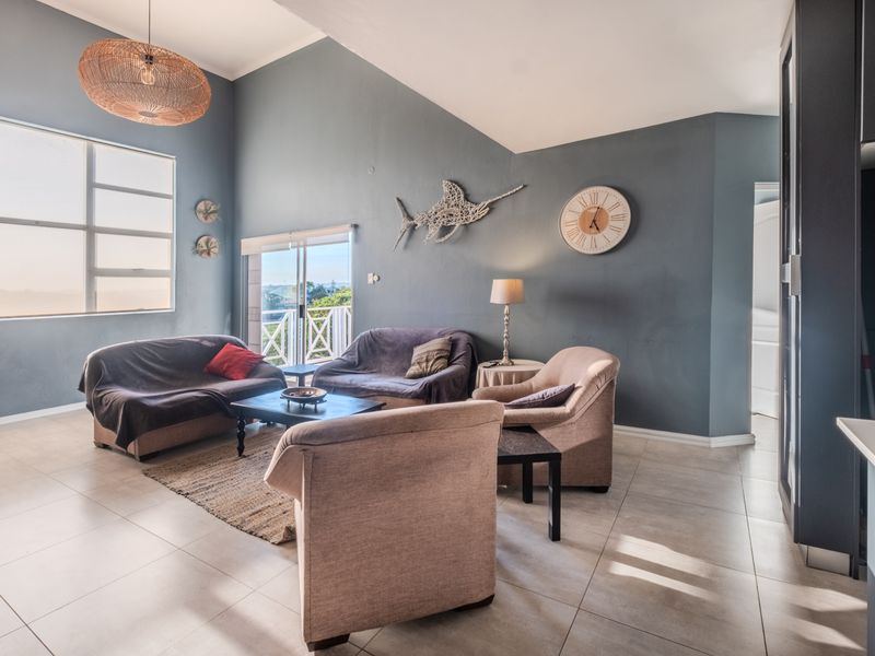 Spacious living room featuring vaulted ceilings, tiled flooring, and large windows with access to a balcony, offering a bright and open atmosphere.