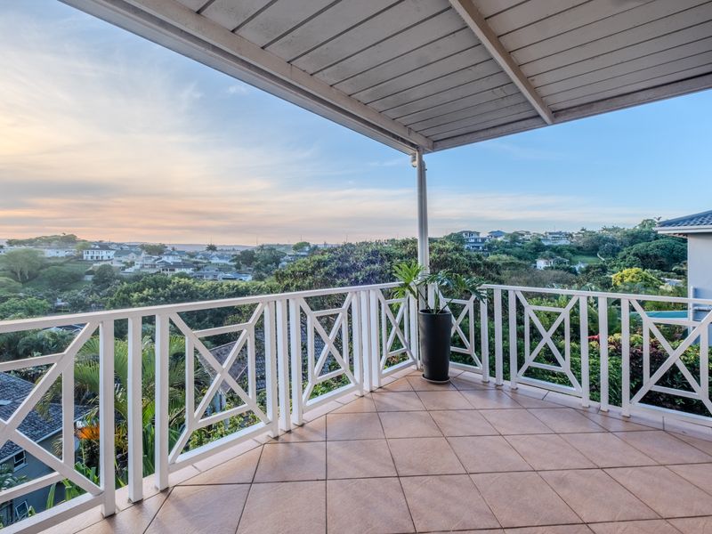 A spacious covered balcony featuring tiled flooring and a white timber balustrade, offering expansive elevated views of the surrounding neighborhood.