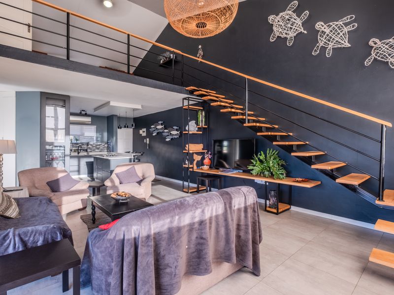 Spacious open-plan living area featuring a modern staircase leading to a mezzanine level, tiled floors, and a contemporary kitchen with an island.