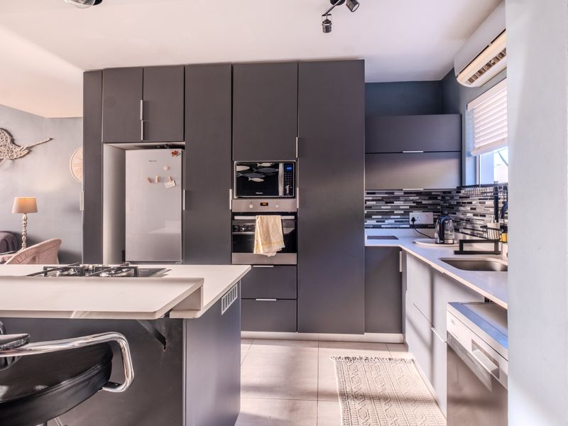 Modern kitchen featuring dark grey cabinetry, a central island with a gas hob, built-in appliances, and a stylish mosaic tile backsplash.