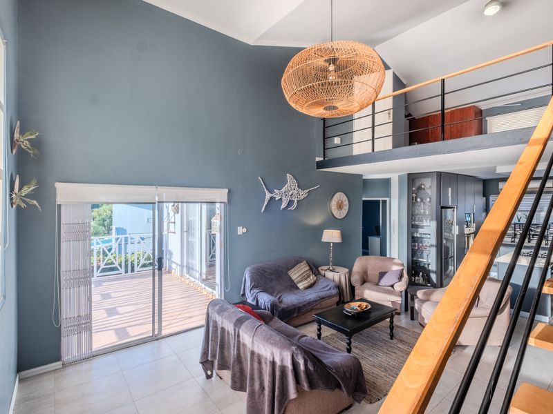 Spacious open-plan living area featuring a mezzanine level, high vaulted ceilings, tiled flooring, and direct access to an outdoor balcony through sliding glass doors.