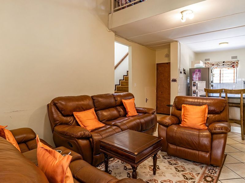 Open-plan living and kitchen area featuring tiled flooring, a breakfast bar, and a staircase leading to an upper level.