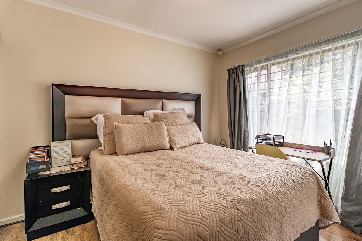 A well-lit bedroom featuring neutral wall tones, cove cornicing, and a large window with security bars, providing a comfortable and functional living space.