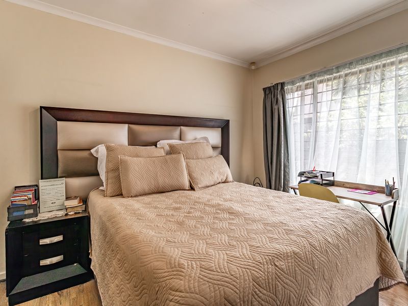 A well-lit bedroom featuring neutral wall tones, cove cornicing, and a large window with security bars, providing a comfortable and functional living space.