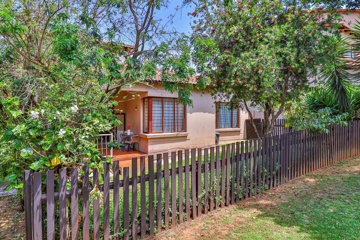 A view of the rear exterior featuring a tiled patio, bay windows with security bars, and a timber picket fence set within a garden.