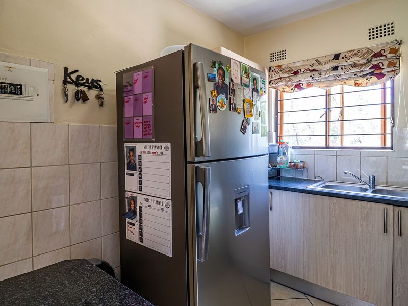 A functional kitchen featuring light-toned cabinetry, dark laminate countertops, a stainless steel sink, and tiled splashbacks, with a window providing natural light.