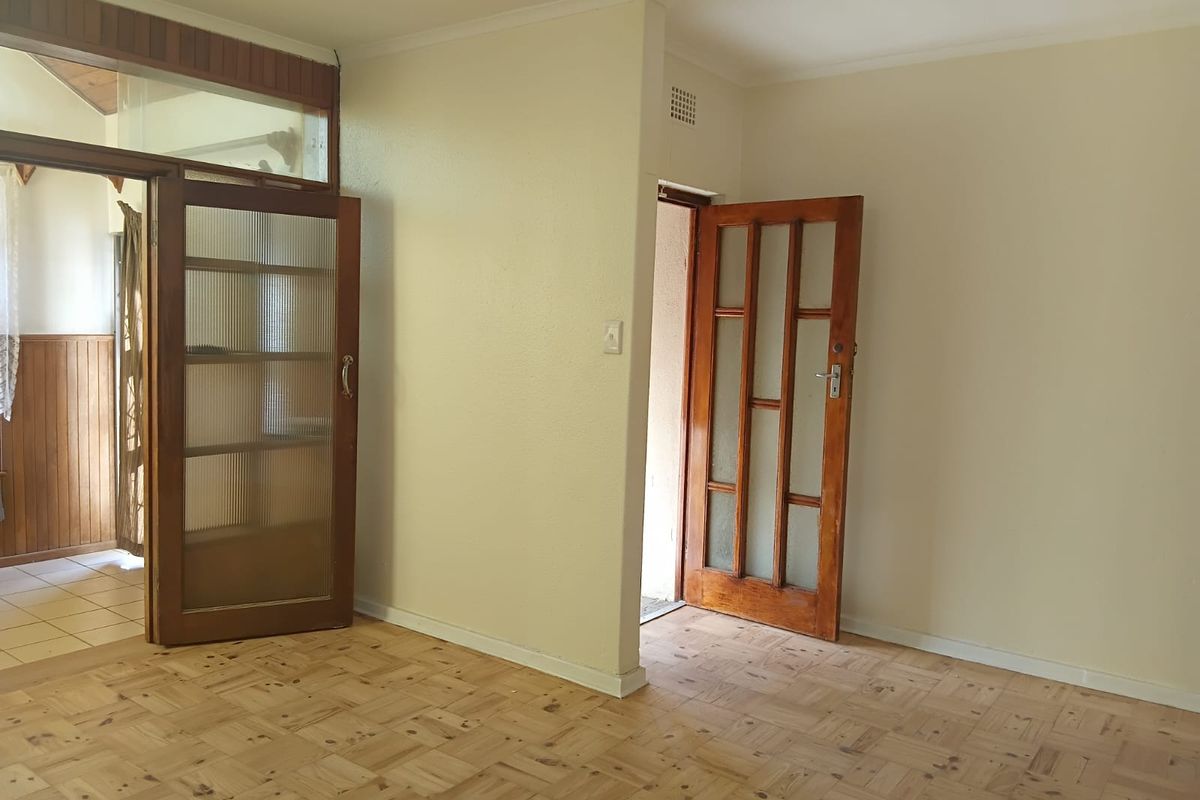 An empty living area featuring classic parquet flooring and timber-framed glass doors, offering a neutral canvas for renovation or interior design updates.
