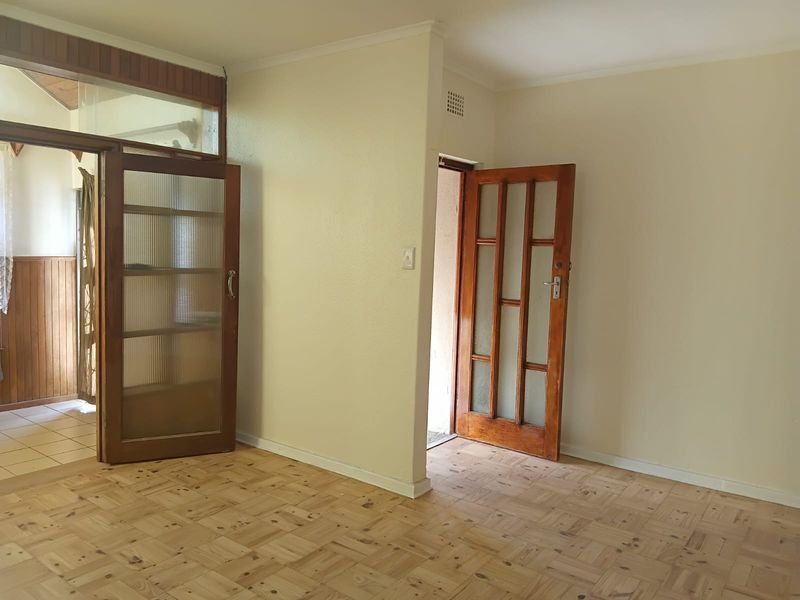 An empty living area featuring classic parquet flooring and timber-framed glass doors, offering a neutral canvas for renovation or interior design updates.