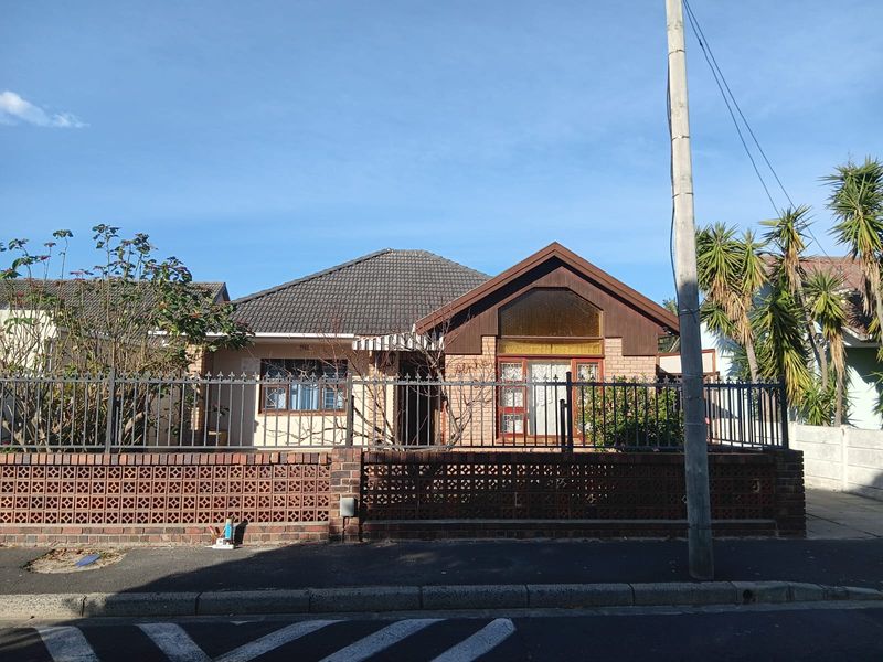Front elevation of a single-story house featuring a tiled roof, decorative brick boundary wall, and metal security fencing.