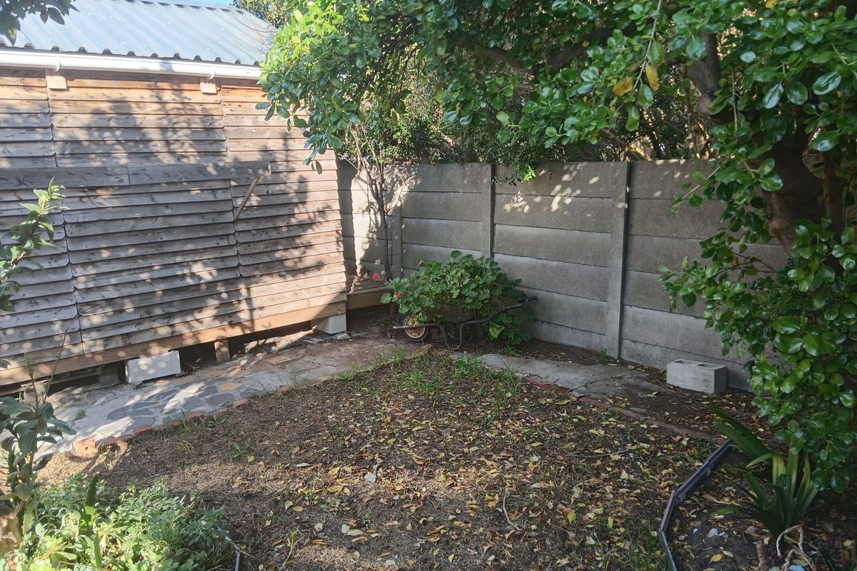 A rear garden area featuring timber-clad structure, precast concrete boundary walls, and stone paving, requiring landscaping and maintenance.