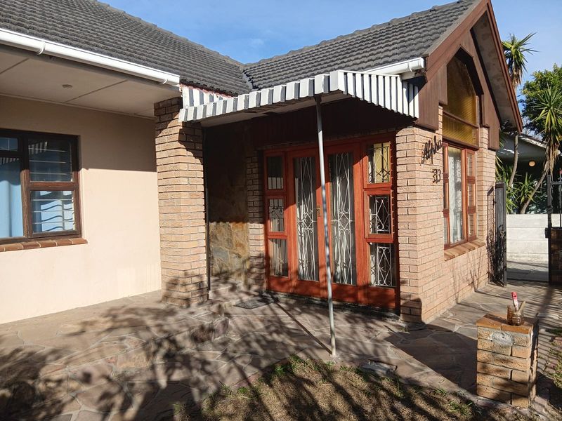 Front entrance of a brick-faced house featuring a stone-paved patio, timber-framed doors with security gates, and a covered awning area.