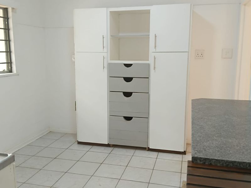 A functional kitchen area featuring built-in storage cabinetry, tiled flooring, and a stone countertop, providing a clean and practical workspace.