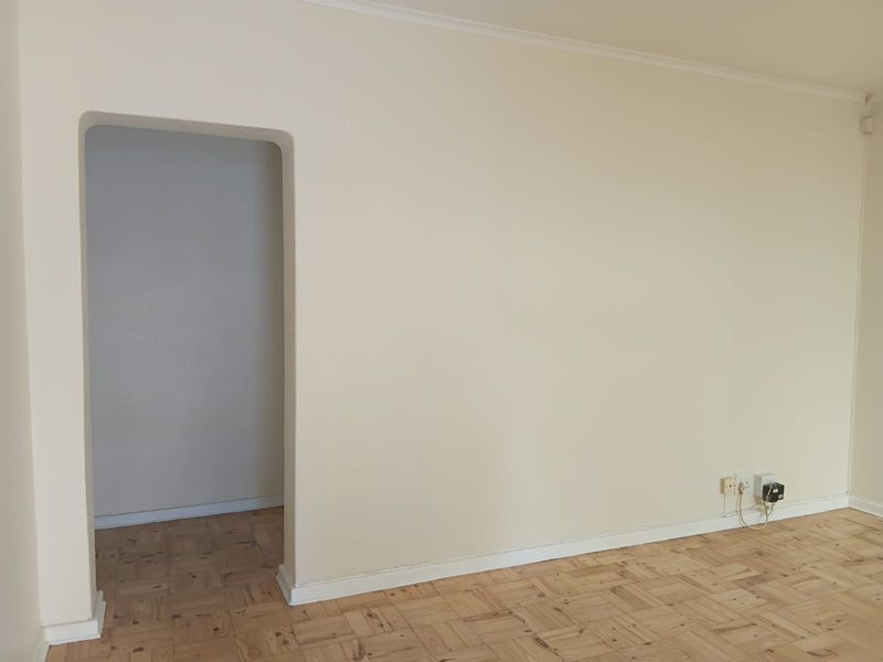 A bright, empty living room featuring classic parquet flooring, a decorative coved ceiling, and a distinctive arched doorway leading to an adjacent space.